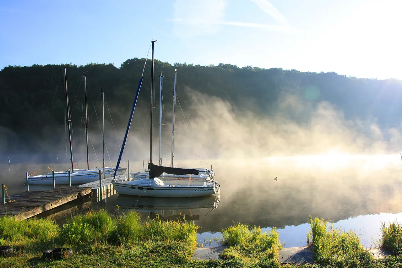 Morning mist rising off Bostalsee beside a wooden jetty